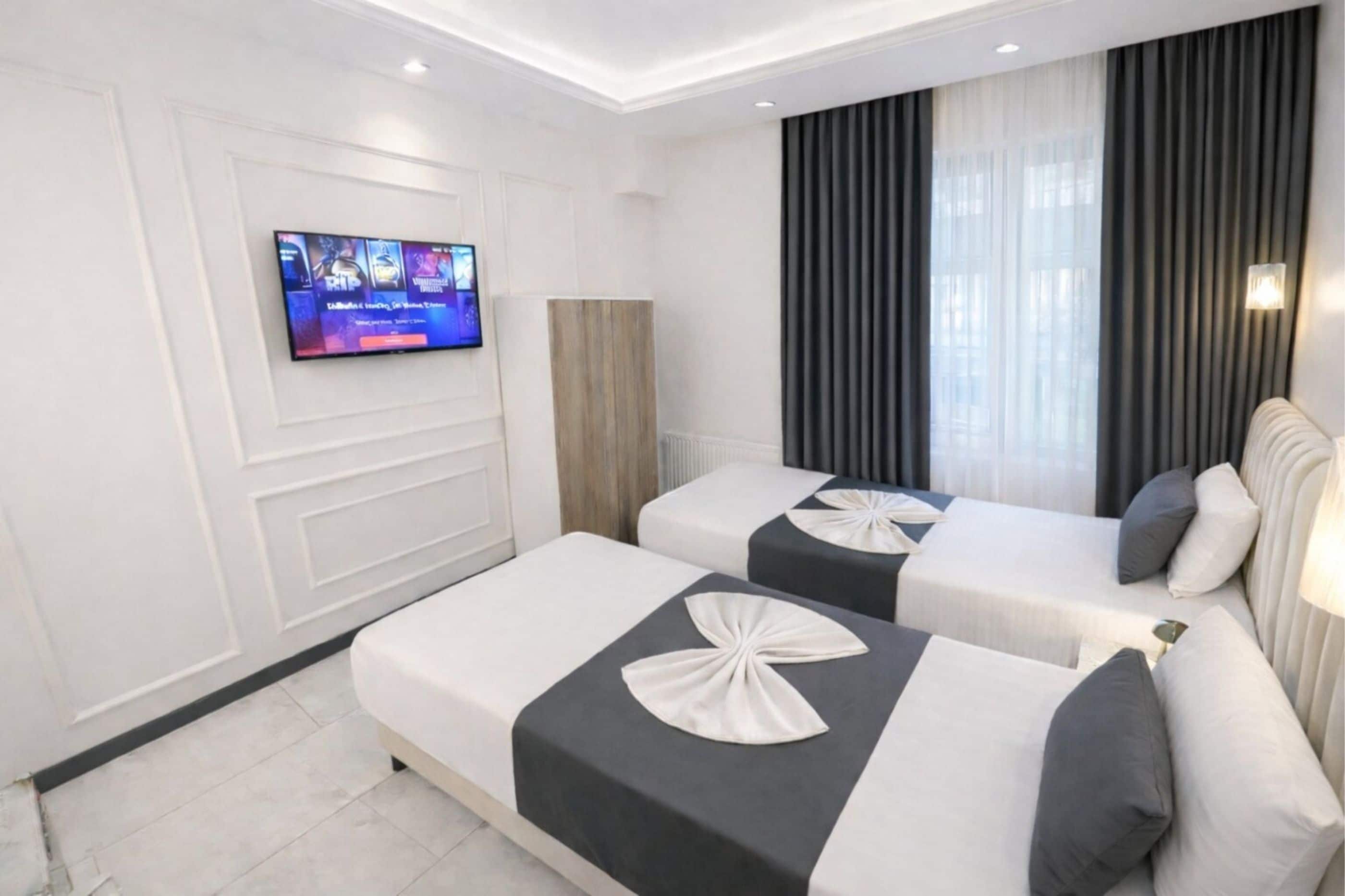 A hotel room with two beds, a TV on the wall, and a large window with curtains.