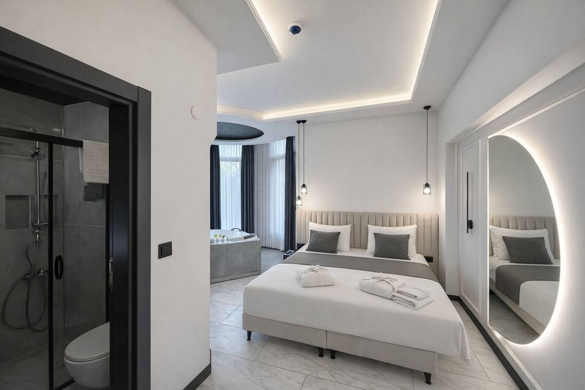 Una habitación de hotel moderna con una cama grande, una zona de estar, un baño con ducha y un espejo amplio.