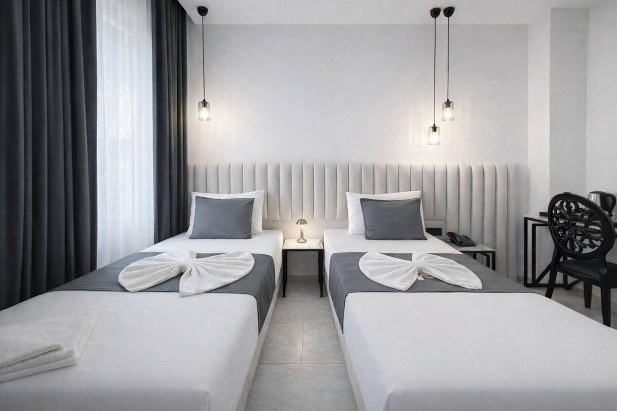 Habitación de hotel con dos camas, un escritorio, una silla y una mesita de noche con lámpara.