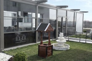 A modern building with large windows, a wooden gazebo, and a white fountain. - D Twins plus Hotel (Arnavutköy)