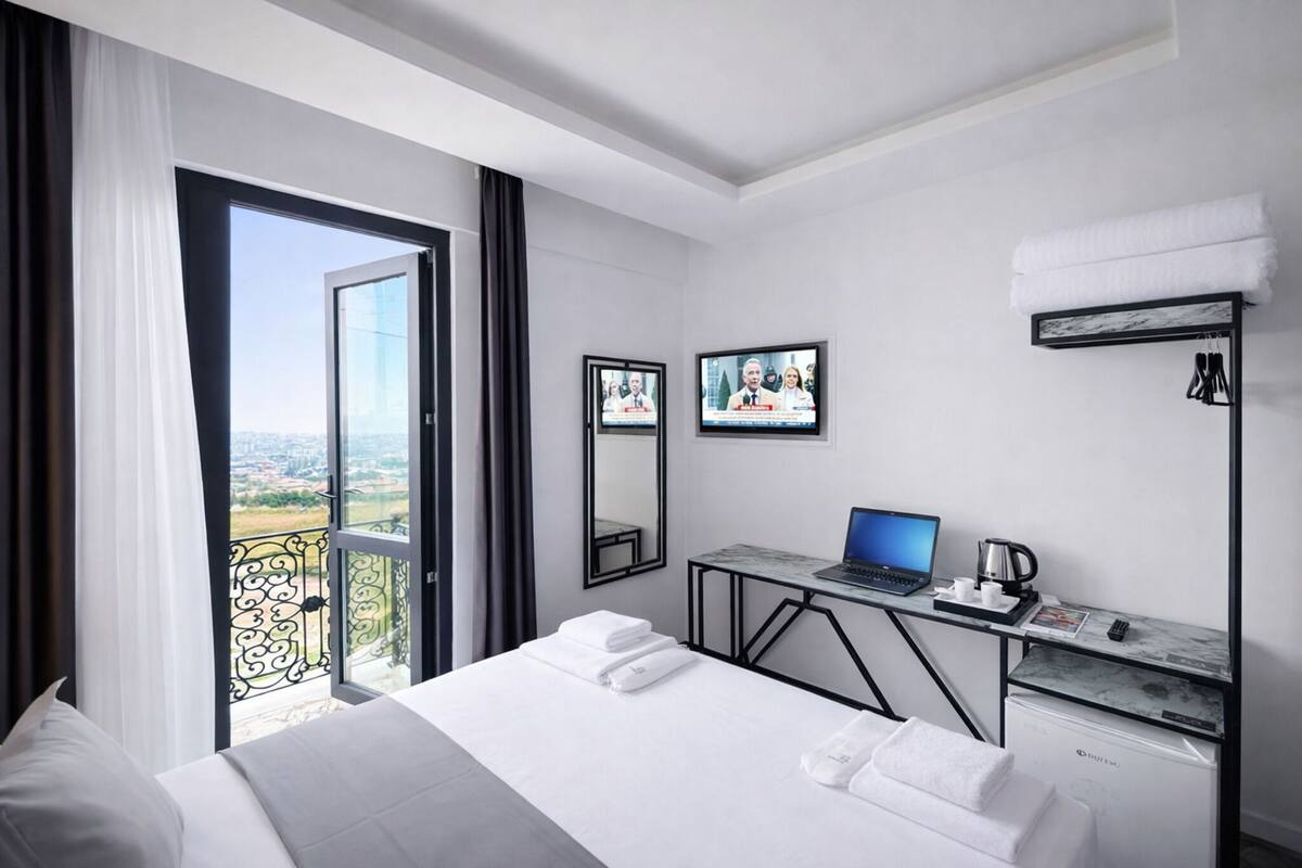Habitación de hotel con una cama, un escritorio con una computadora portátil, una cafetera y un televisor.