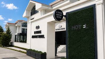 Un edificio moderno con un cartel que dice 'D Twins Airport Hotel' y una amplia entrada de cristal.