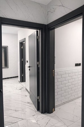 A hallway with white brick walls, a marble floor, and black-framed doors. - D Twins plus Hotel (Arnavutköy)
