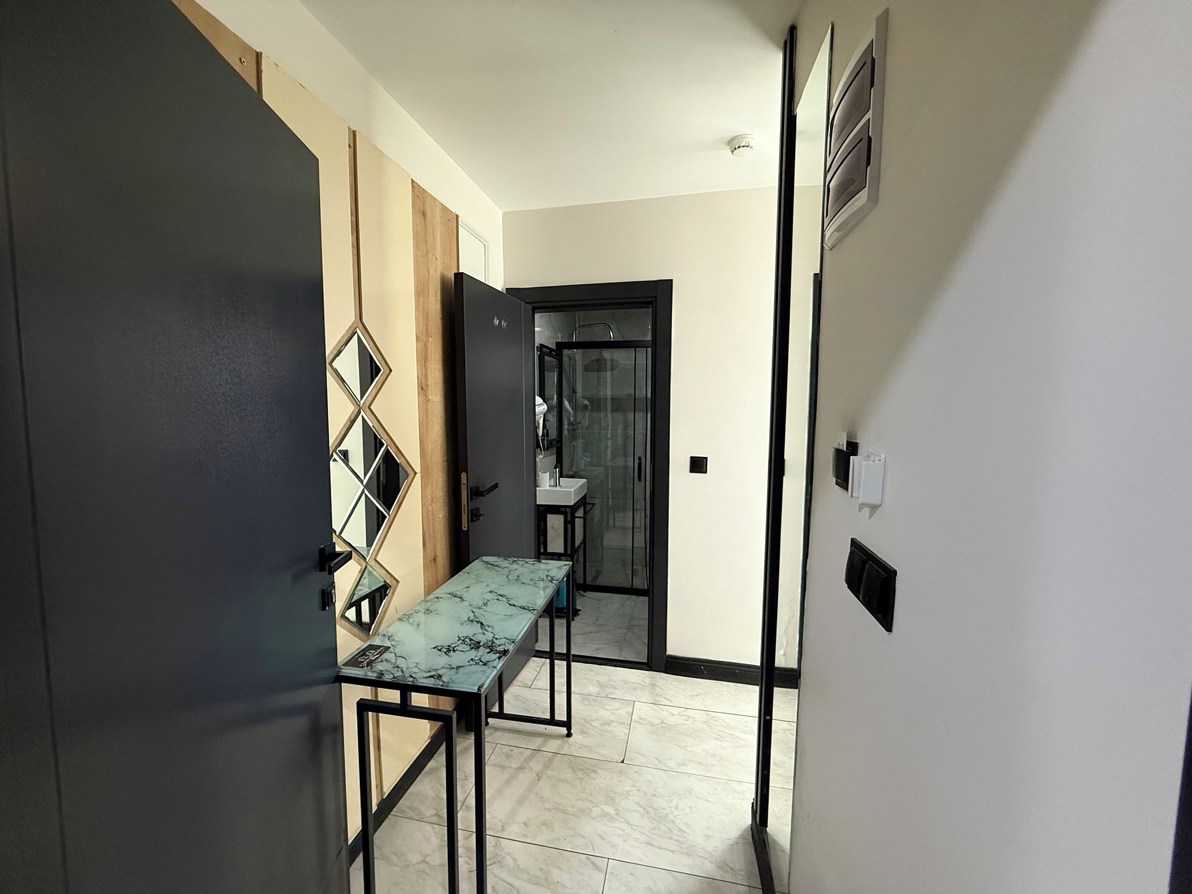 Un pasillo con una mesa de mármol, una puerta con espejo y un baño visible a través de una puerta abierta.