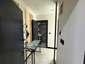 Un couloir avec une table surmontée d’un plateau en marbre, une porte dotée d’un miroir et une salle de bain visible à travers une porte ouverte.