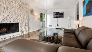 Una sala de estar moderna con pared de piedra, chimenea, mesa de centro de vidrio, sofás de cuero y televisor montado.