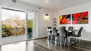 Un comedor moderno con una puerta corrediza de vidrio que da a un balcón, una mesa de comedor con sillas y arte abstracto en la pared.