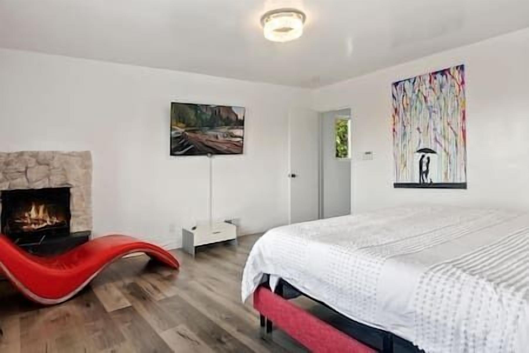 A modern bedroom with a fireplace, a bed with a white cover, and two artworks on the walls.