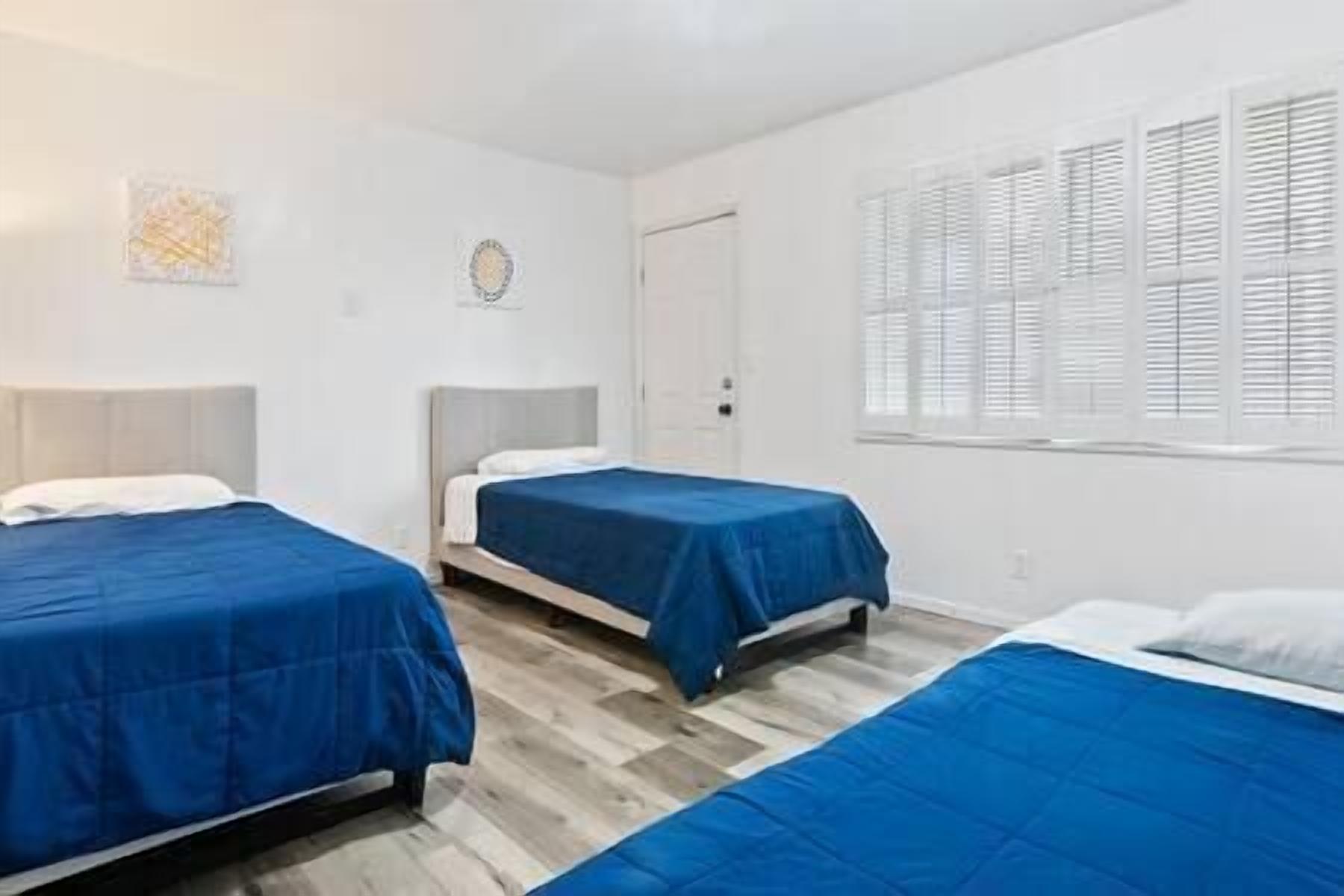 Habitación de hotel con dos camas individuales, suelo de madera, puerta blanca y ventana con persianas.