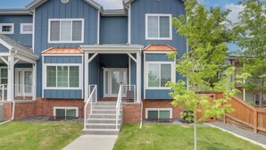 A two-story residential building with a front porch, a brick foundation, and a small tree in the front yard.