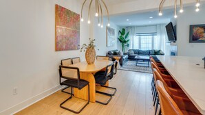 A modern living room with a dining area, a sofa, a TV, and artwork on the walls.