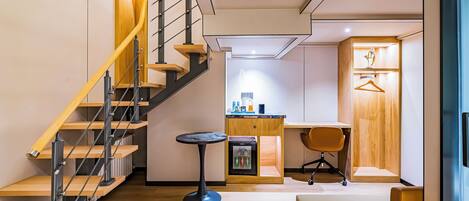 A modern interior with a wooden staircase, a small kitchenette, a seating area, and a wooden door.