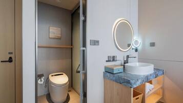 A modern bathroom with a toilet, a sink with a marble countertop, and a mirror with a circular light.