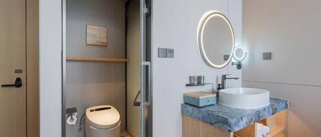 Un baño moderno con inodoro, lavamanos con encimera de mármol y espejo con luz circular.