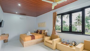 Ein Schlafzimmer mit einem Bett, zwei Stühlen, einem kleinen Tisch und einem Fenster mit Blick auf Palmen.