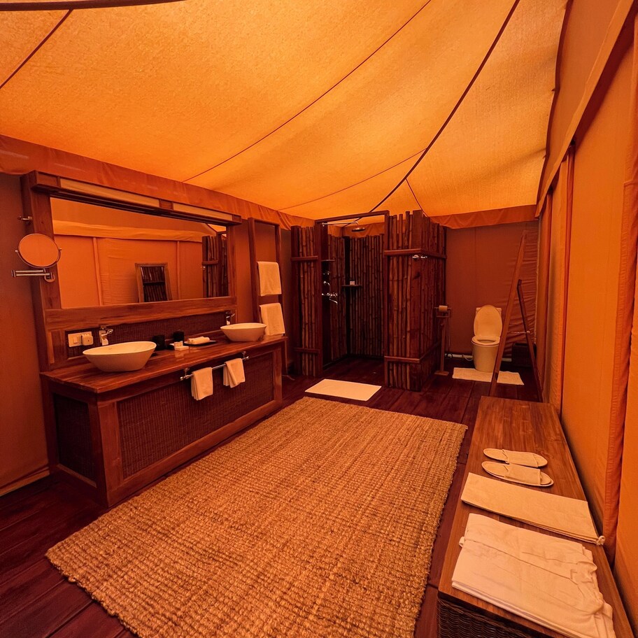 A tented room with a wooden vanity, two sinks, a mirror, and a large woven rug.