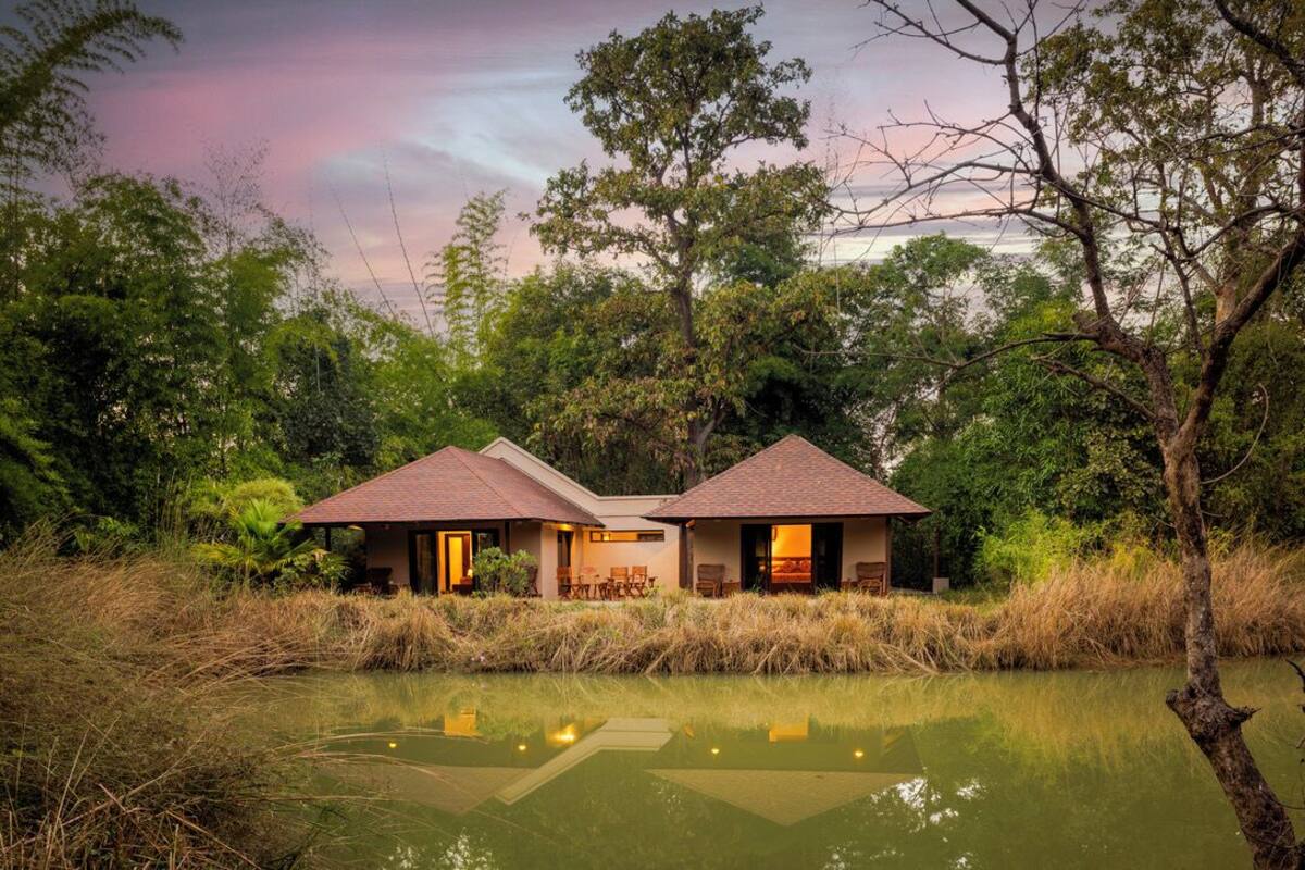 A bungalow with a tiled roof, surrounded by lush greenery and a body of water.