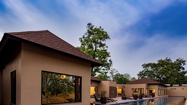 A modern pool area with lounge chairs and a view of the surrounding landscape. - Bagh Villas | Kanha (Baihar)