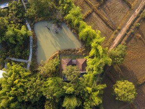 An aerial view of a property with a pond, dense greenery, and a small building with a sloped roof.