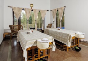 A room with two beds, wooden furniture, and large windows with curtains.