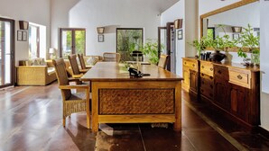 A spacious dining area with a long wooden table, wicker chairs, and a wooden cabinet with drawers. - Bagh Villas | Kanha (Baihar)