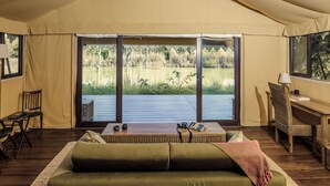 A tent with a wooden deck, a sofa, a table, and a chair. - Bagh Villas | Kanha (Baihar)