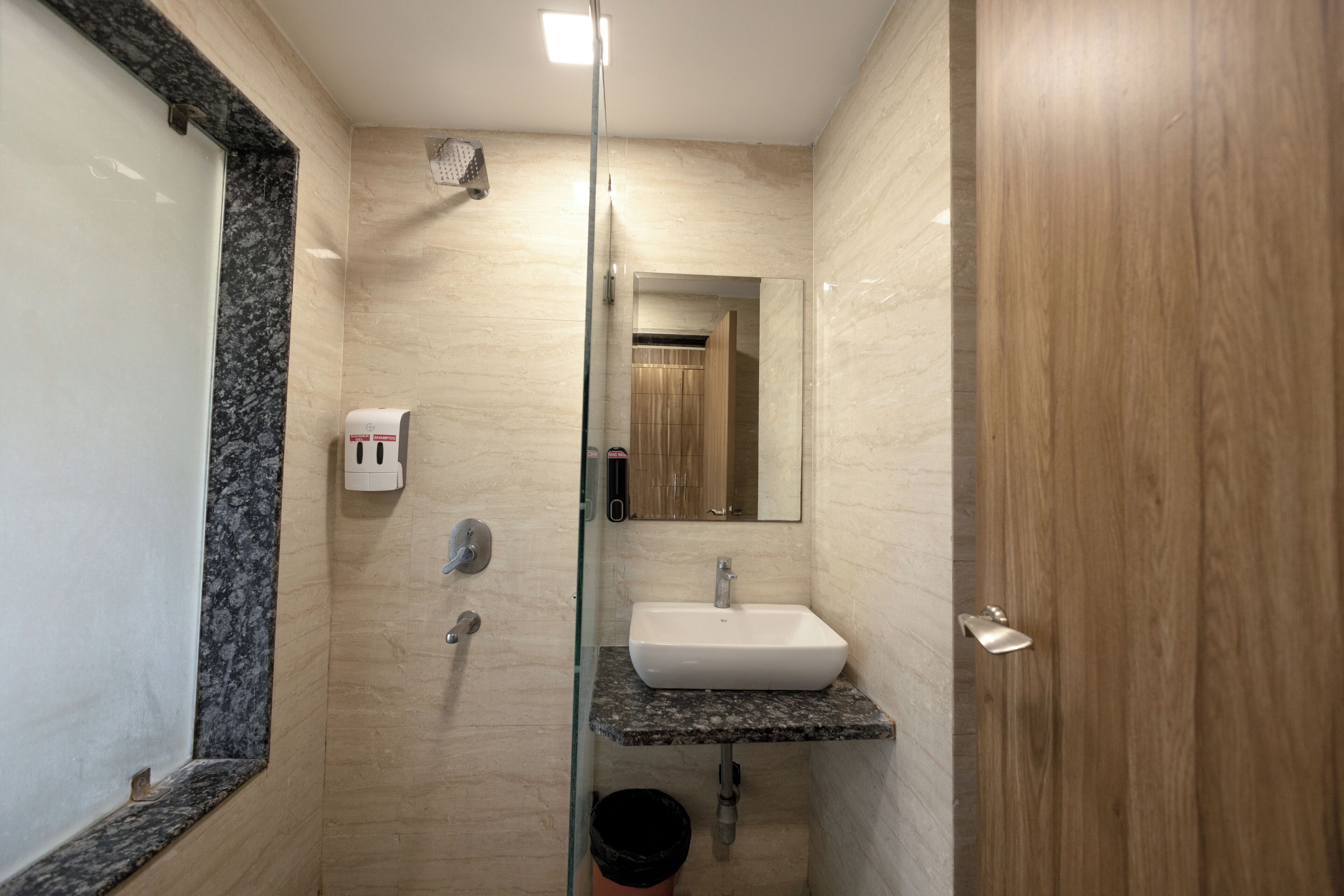 A bathroom with a glass shower enclosure, a marble countertop sink, a mirror, and a wooden door.