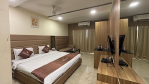 A hotel room with a large bed, a desk, a television, and an air conditioning unit. - Hotel Vikramaditya (Ujjain)
