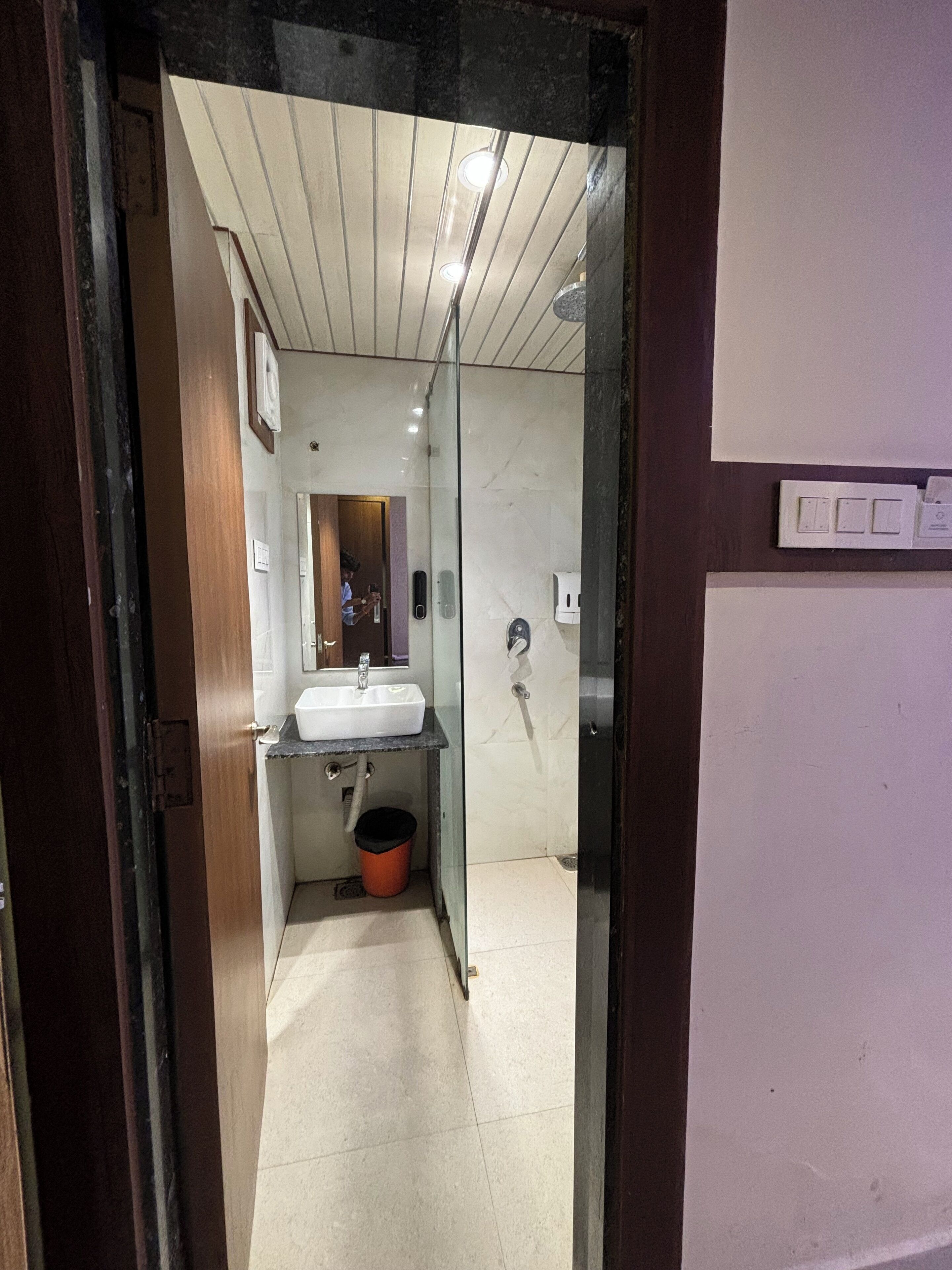 Un corridoio stretto che porta a un bagno con lavandino, specchio e cabina doccia in vetro.