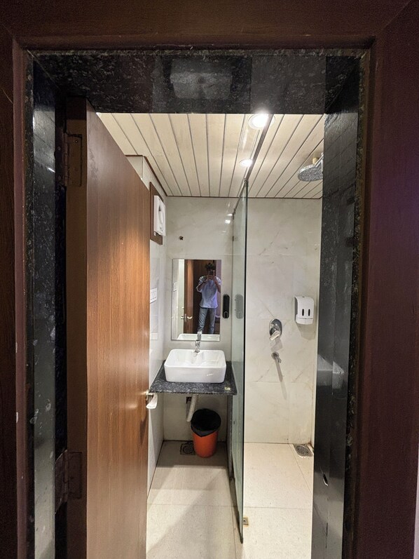 Een smalle gang die uitkomt bij een badkamer met een wastafel, spiegel en douche.