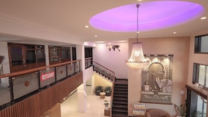 A spacious lobby with a staircase, a reception desk, and a wall with decorative elements. - Hotel Vikramaditya (Ujjain)