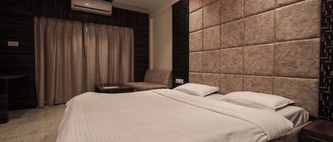 A modern hotel room with a large bed, a seating area, and a built-in air conditioning unit.