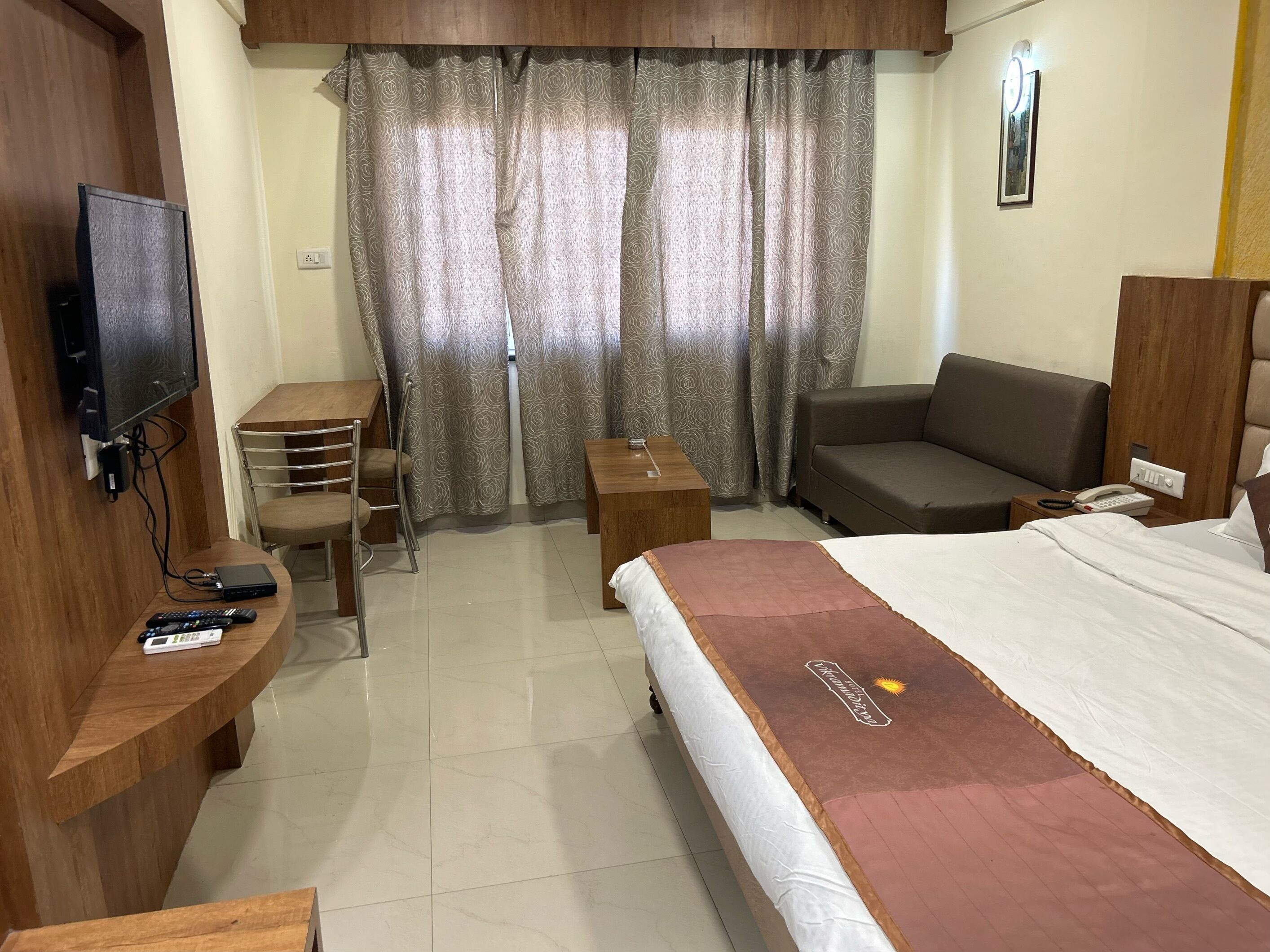 Ein Hotelzimmer mit Bett, Schreibtisch mit Stuhl, Sofa, Fernseher und Vorhängen.