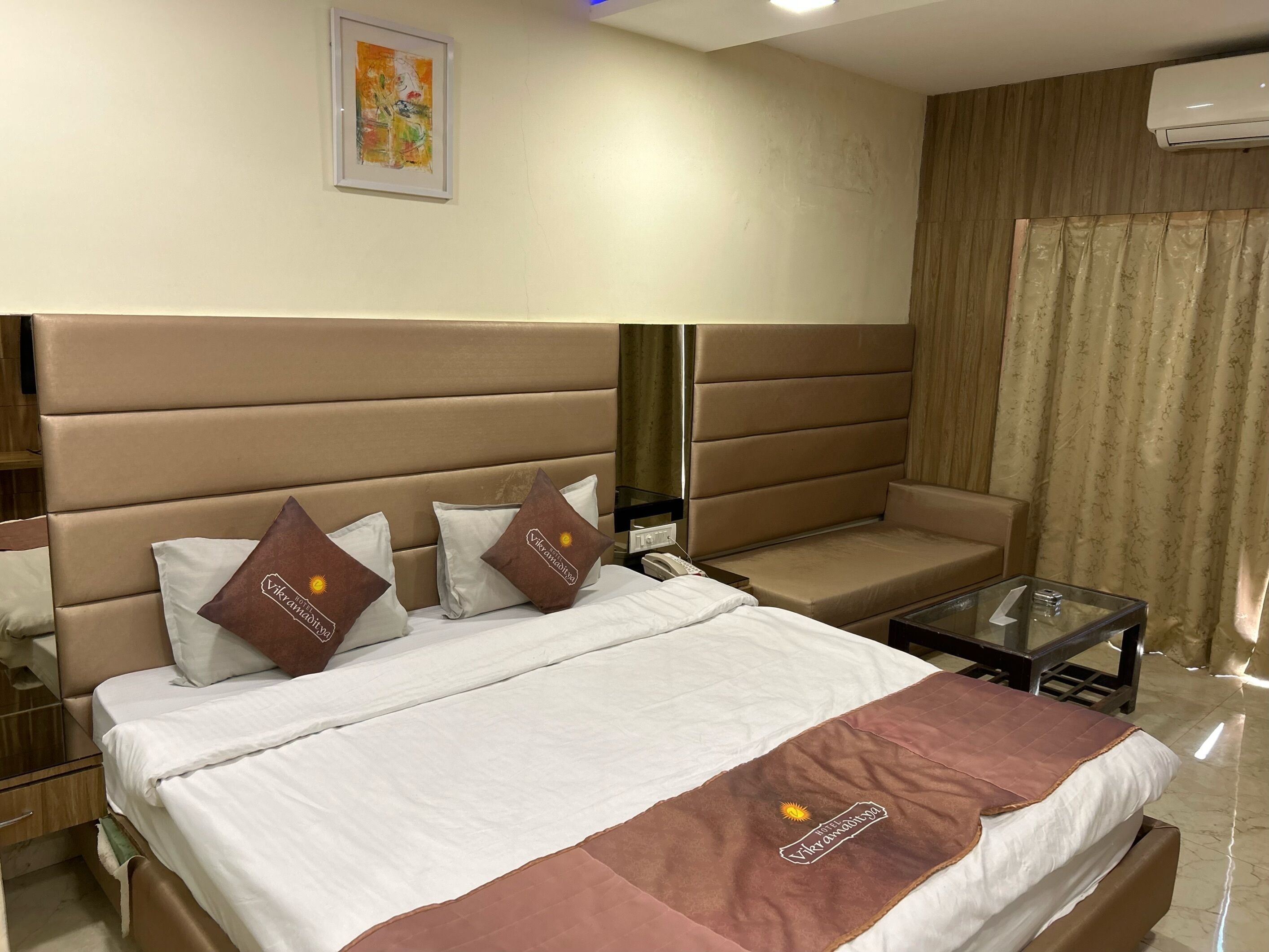 Ein Hotelzimmer mit einem großen Bett, zwei Kissen, einer kleinen Couch, einem Glastisch und einem Bild an der Wand.