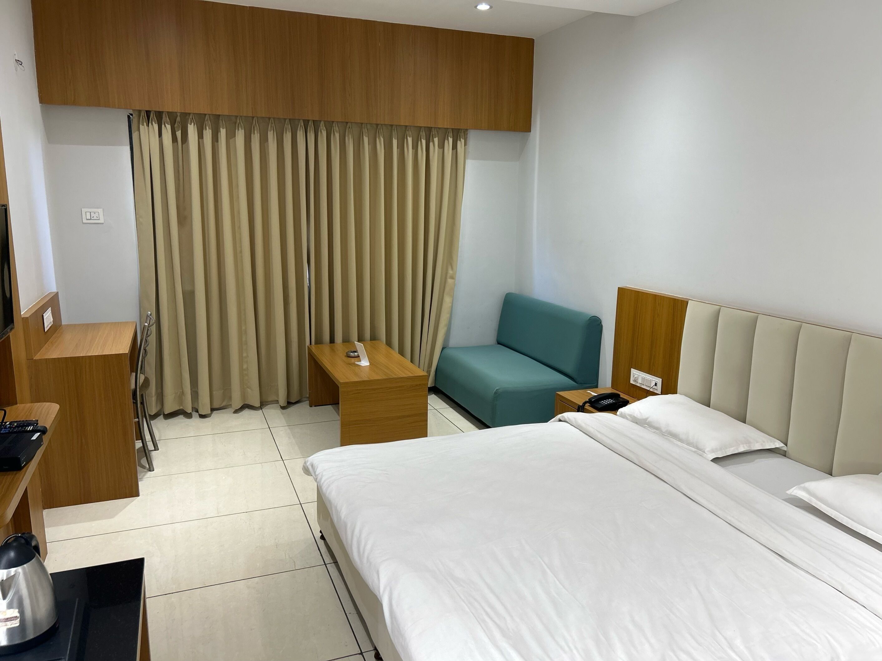 A hotel room with a bed, a desk, a chair, a telephone, and a kettle.
