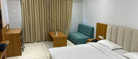 A hotel room with a bed, a desk, a chair, a telephone, and a kettle.