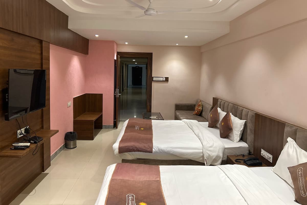 A hotel room with two beds, a desk, a TV, and a ceiling fan.