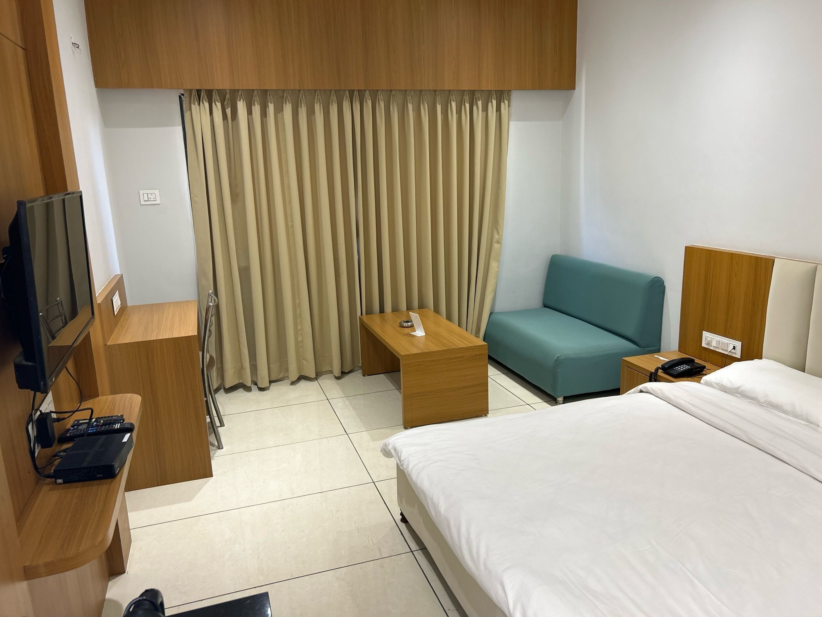 A hotel room with a bed, a desk, a television, a sofa, and a curtain.