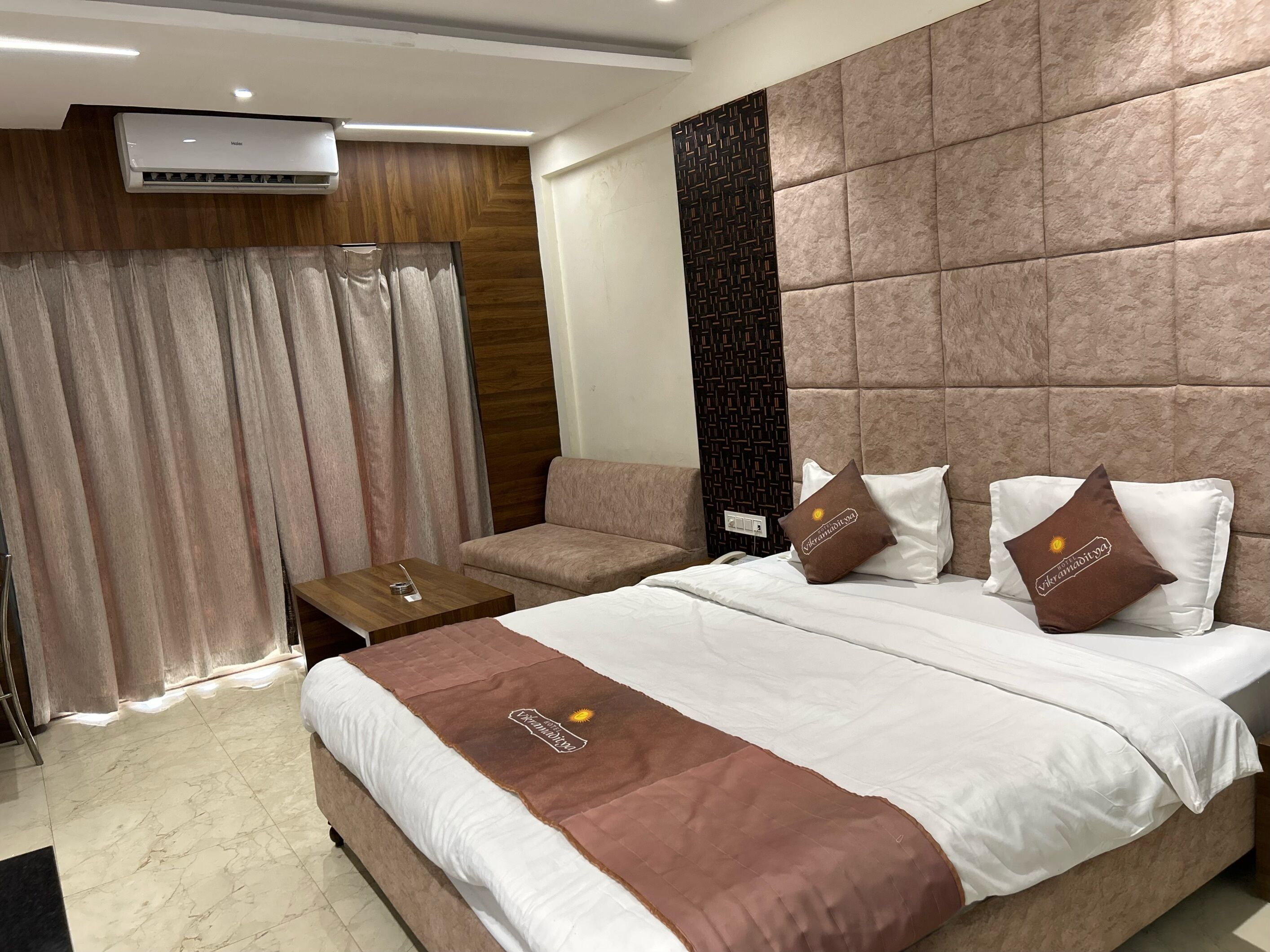 Habitación de hotel con una cama grande, un sofá, una mesita y un aire acondicionado instalado en la pared.