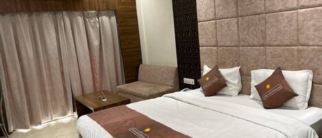 Habitación de hotel con una cama grande, un sofá, una mesita y un aire acondicionado instalado en la pared.