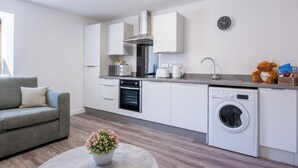 Eine moderne Küche mit weißen Schränken, einem eingebauten Backofen, einer Mikrowelle, einer Kaffeemaschine und einer Waschmaschine.