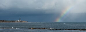 Un faro sobre un promontorio rocoso con un arcoíris en el fondo.
