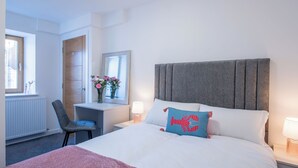 Hotellihuone, jossa on sänky, yöpöydät, tuoli, työpöytä, peili ja ikkuna.