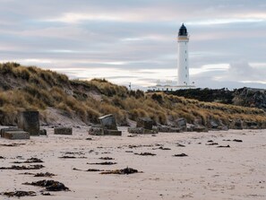 Ein Leuchtturm an einem sandigen Strand mit grasbewachsenen Dünen im Hintergrund.