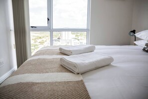 Habitación de hotel con un ventanal grande, una cama con ropa blanca y vistas a edificios.