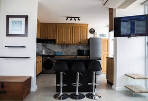 Eine moderne Küche mit Holzschränken, einer Marmor-Spritzschutzwand, einer integrierten Waschmaschine und einer Bar mit drei Hockern.