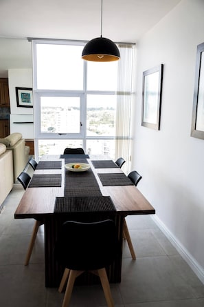 Un espace repas moderne avec une table en bois, des chaises noires et un luminaire suspendu noir.