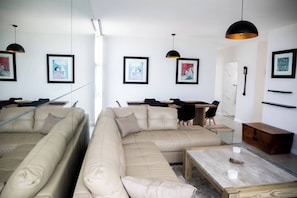 Un salon moderne avec deux canapés beige, une table basse en bois et un coin repas comprenant une table et des chaises.