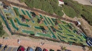 An aerial view of a golf course with multiple green areas, pathways, and wooden structures. - Luxurious 3-bedroom Apartment With Ocean Views in Cape Town (Cape Town)