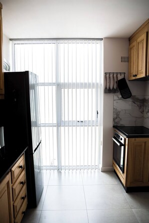 A modern kitchen with a sliding glass door, wooden cabinets, and a black refrigerator. - Luxurious 3-bedroom Apartment With Ocean Views in Cape Town (Cape Town)